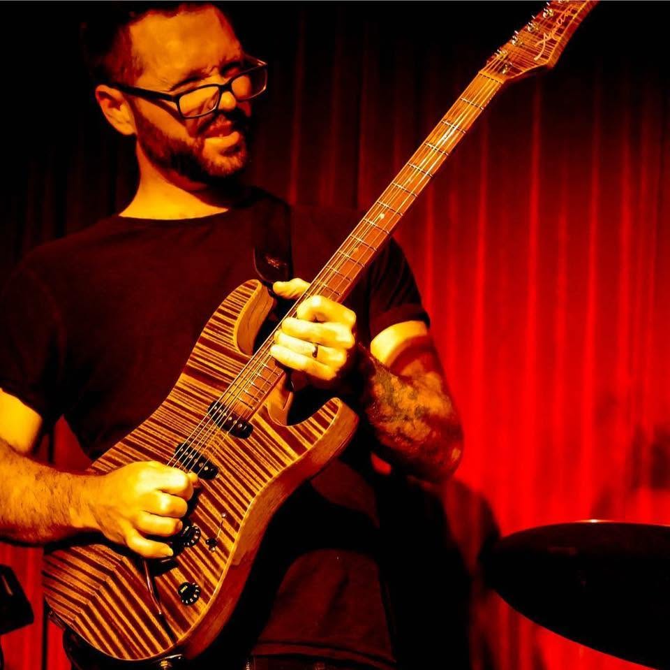Conrad Bauer playing electric guitar on stage under red light